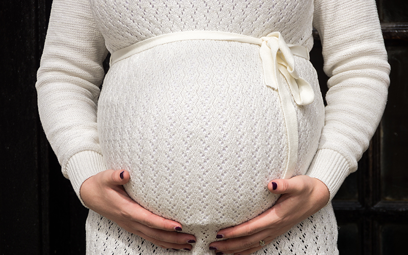 Une femme enceinte enveloppe son ventre de ses mains.