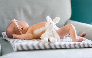 Un bébé allongé sur un canapé avec un lapin en peluche.