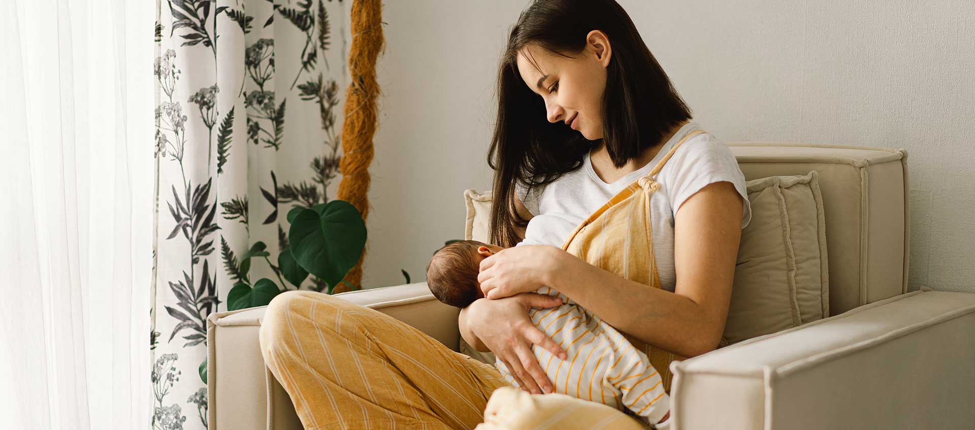 Une maman, installée dans un fauteuil dans son salon, allaite son bébé