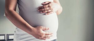 Une femme enceinte enveloppe son ventre de ses deux mains